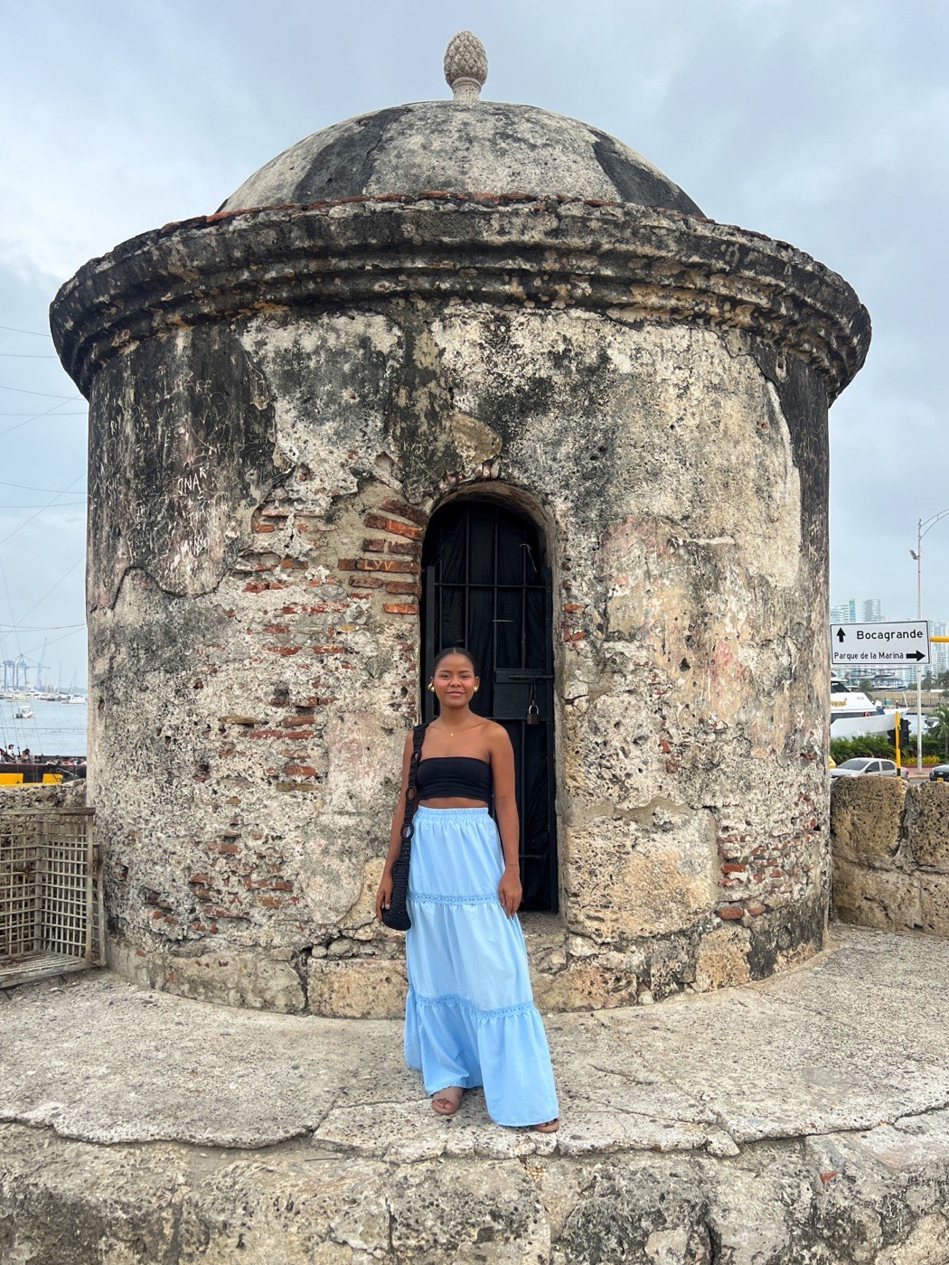 A Black woman in a blue skirt stands in the doorway of an old stone sentry post on Cartagena's city walls